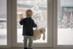 child-with-stuffed-toy-looking-out-the-window-at-a-wintry-scene